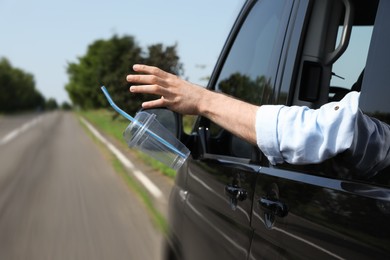 Photo of Driver throwing away plastic cup from car window. Garbage on road