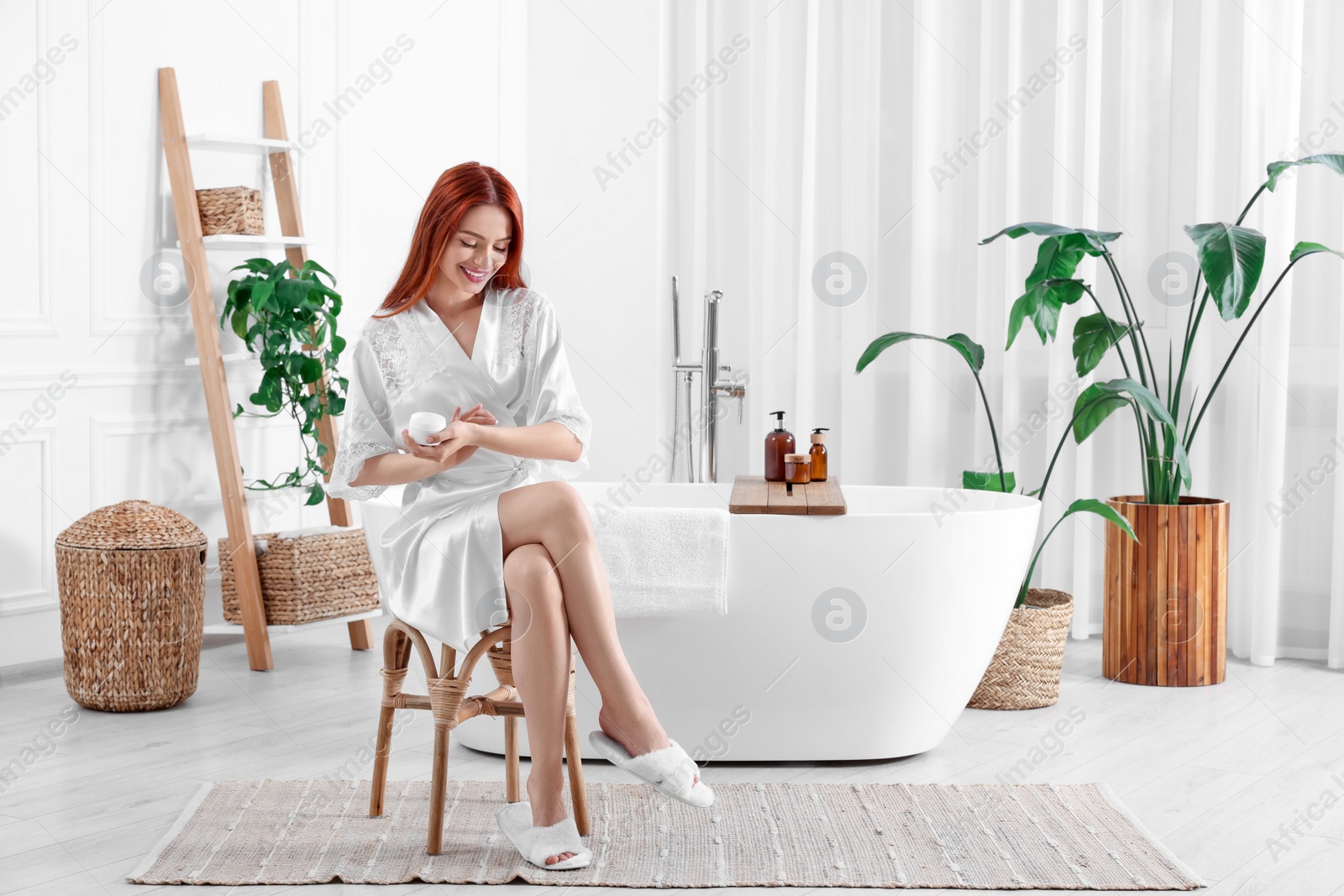 Photo of Beautiful young woman applying body cream onto hands in bathroom, space for text