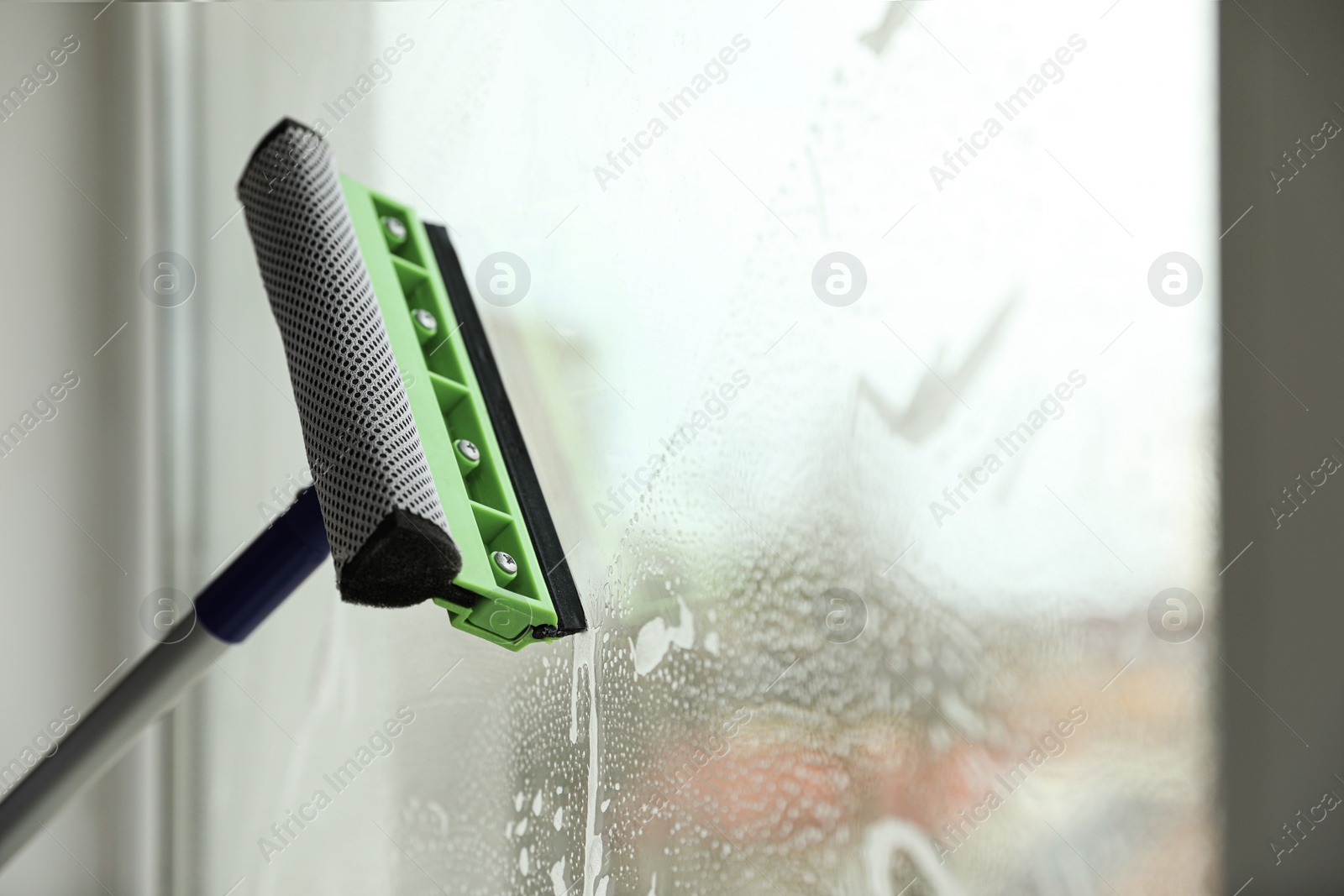 Photo of Cleaning window with squeegee indoors. Space for text