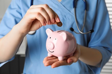 Photo of Doctor putting coin into piggy bank, closeup. Medical insurance