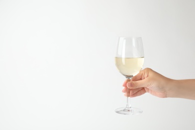 Woman holding glass of expensive white wine on light background