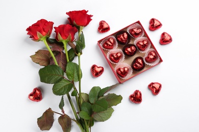 Heart shaped chocolate candies and bouquet on white background, top view