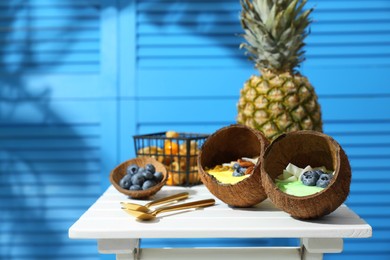 Tasty smoothie bowl served in coconut shells on white wooden table