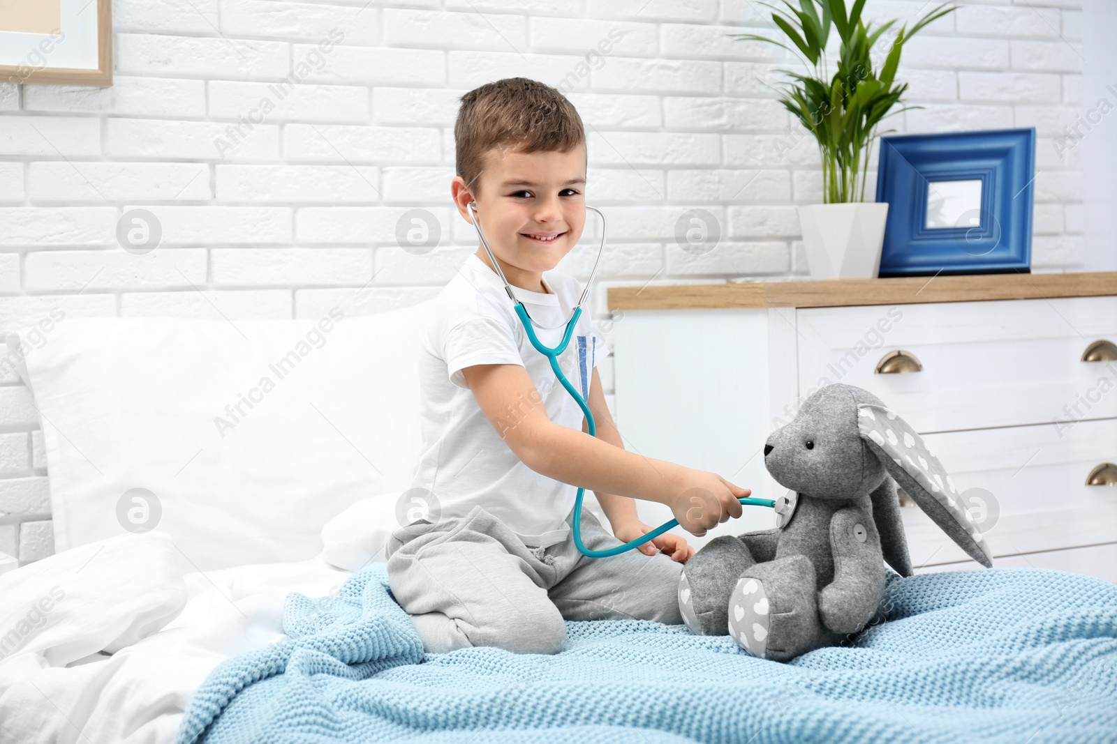 Photo of Cute child playing doctor with stuffed toy on bed in hospital ward