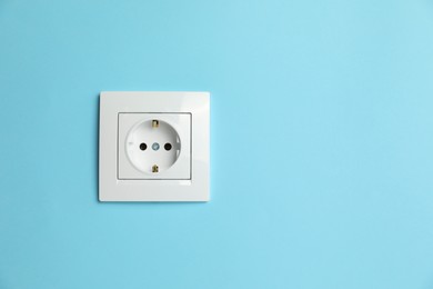 Power socket on light blue wall, space for text. Electrical supply