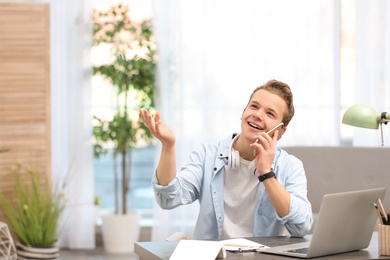 Handsome teenage boy talking on phone at table in room