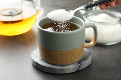 Photo of Woman adding sugar into aromatic tea at grey table, closeup