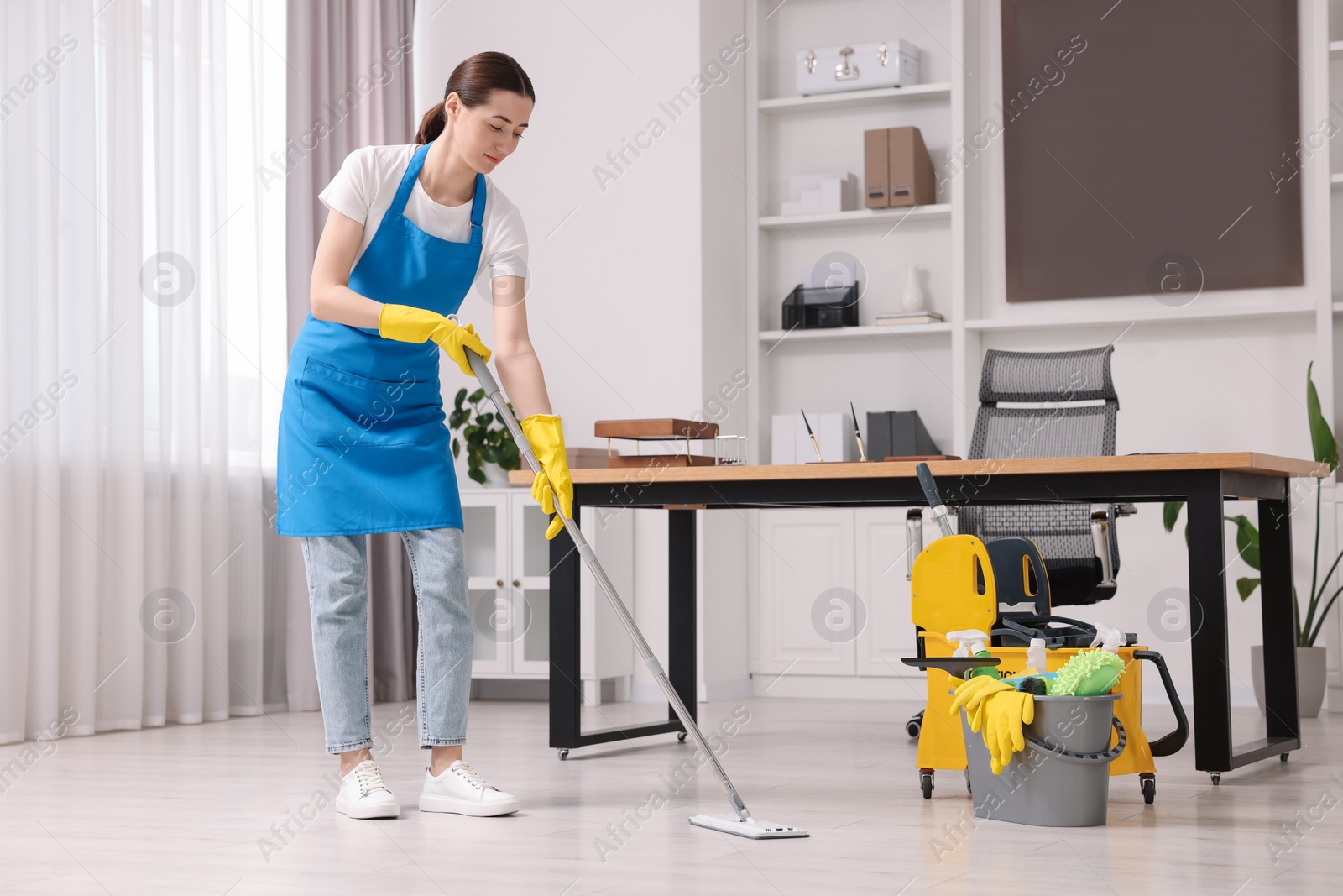 Photo of Cleaning service worker washing floor with mop. Bucket with supplies in office