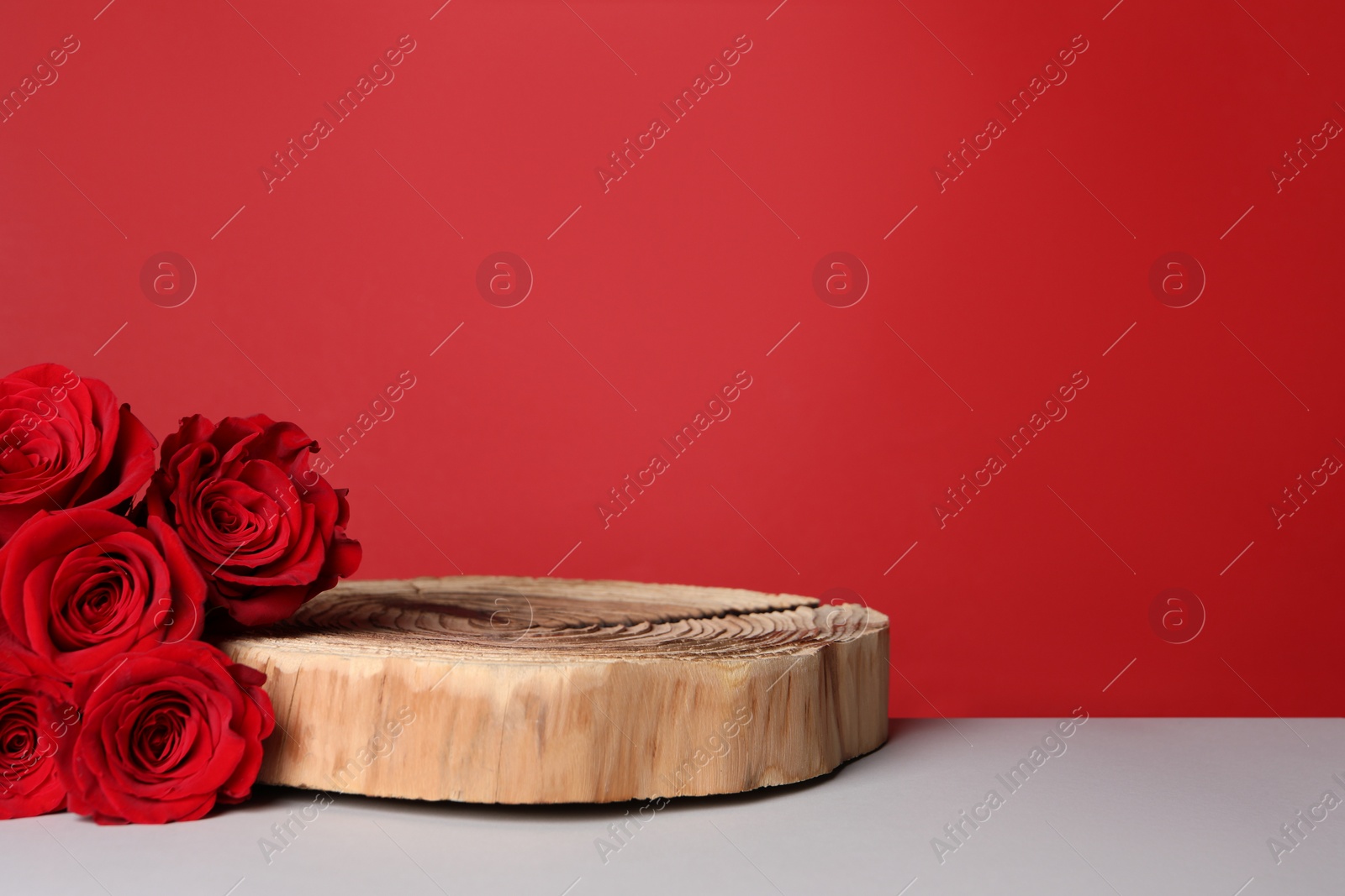 Photo of Presentation for product. Wooden podium and beautiful roses on white table against red background, space for text