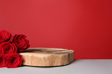 Photo of Presentation for product. Wooden podium and beautiful roses on white table against red background, space for text