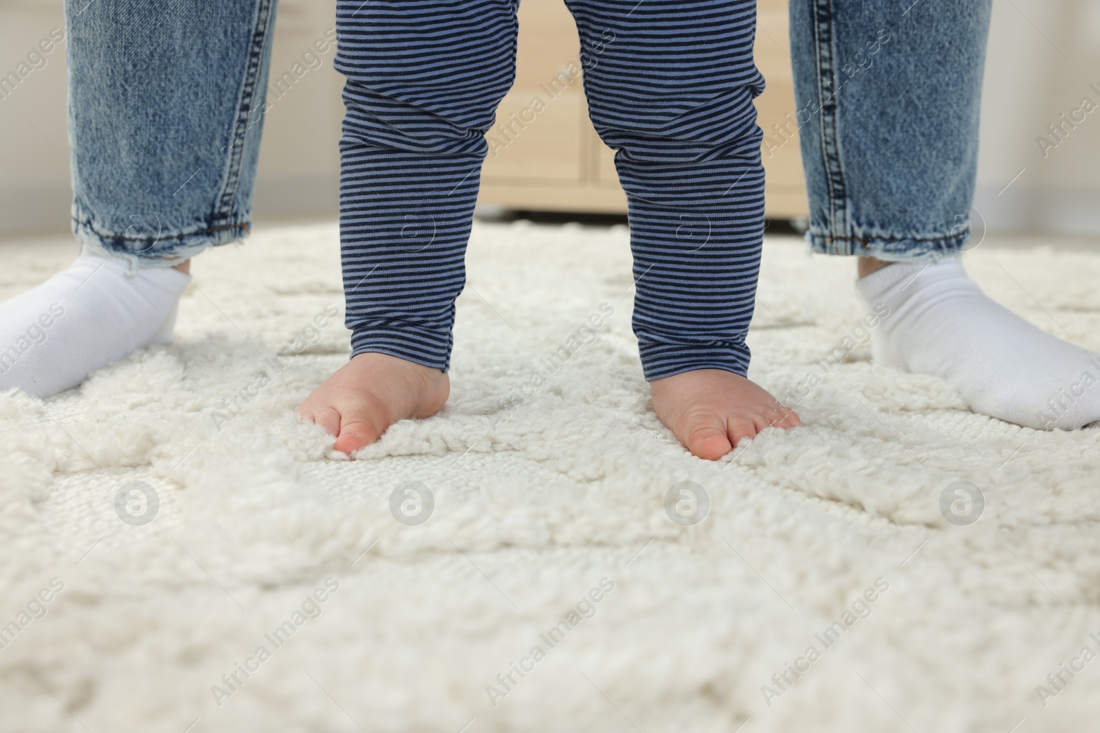 Photo of Mother supporting her son while he learning to walk on carpet indoors, closeup