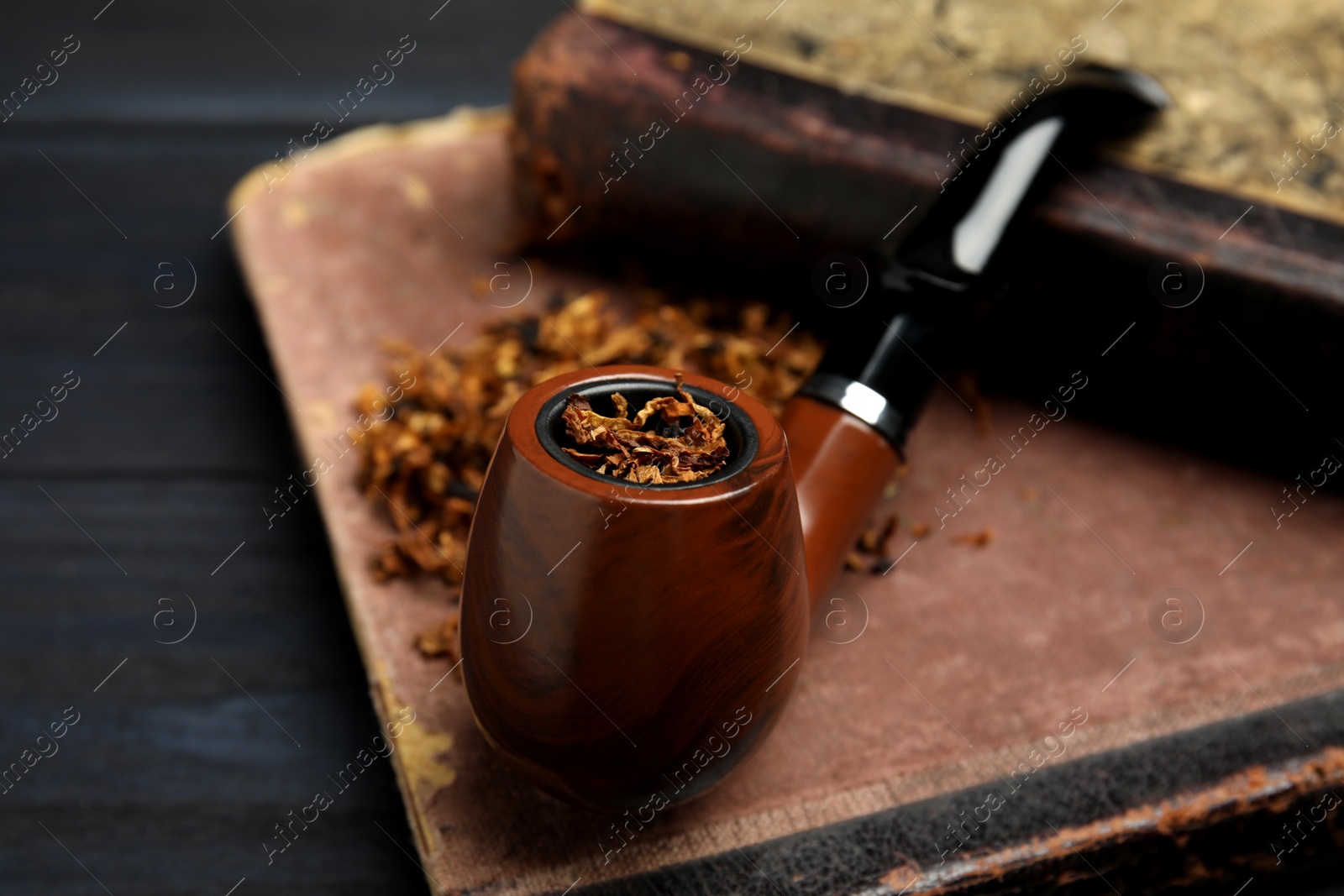 Photo of Smoking pipe, dry tobacco and old books on black table, closeup. Space for text