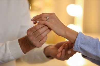 Photo of Making proposal. Man putting engagement ring on his girlfriend's finger against blurred background, closeup