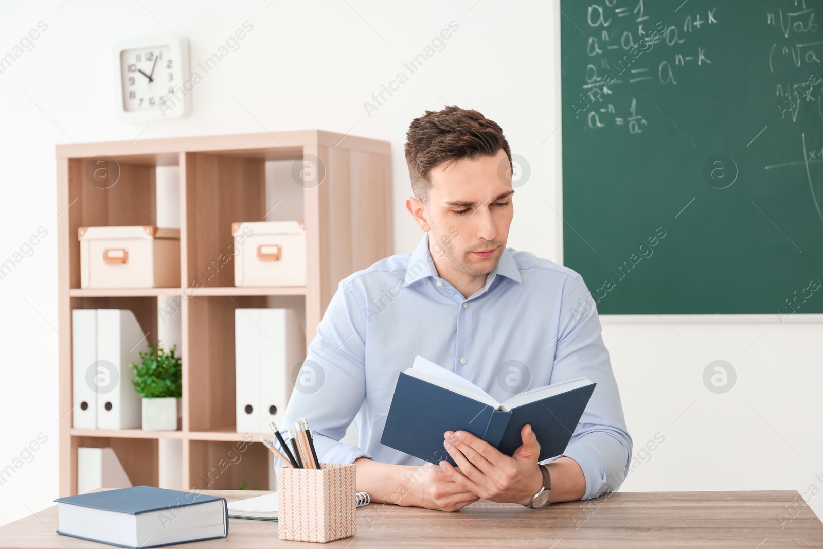 Photo of Young male teacher with notebook sitting at table in classroom