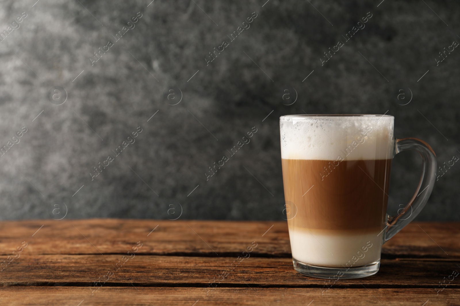 Photo of Glass cup of delicious layered coffee on wooden table against grey background, space for text