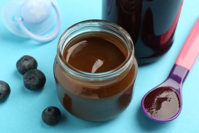 Photo of Jars with healthy baby food, spoon, blueberries and pacifier on light blue background, closeup