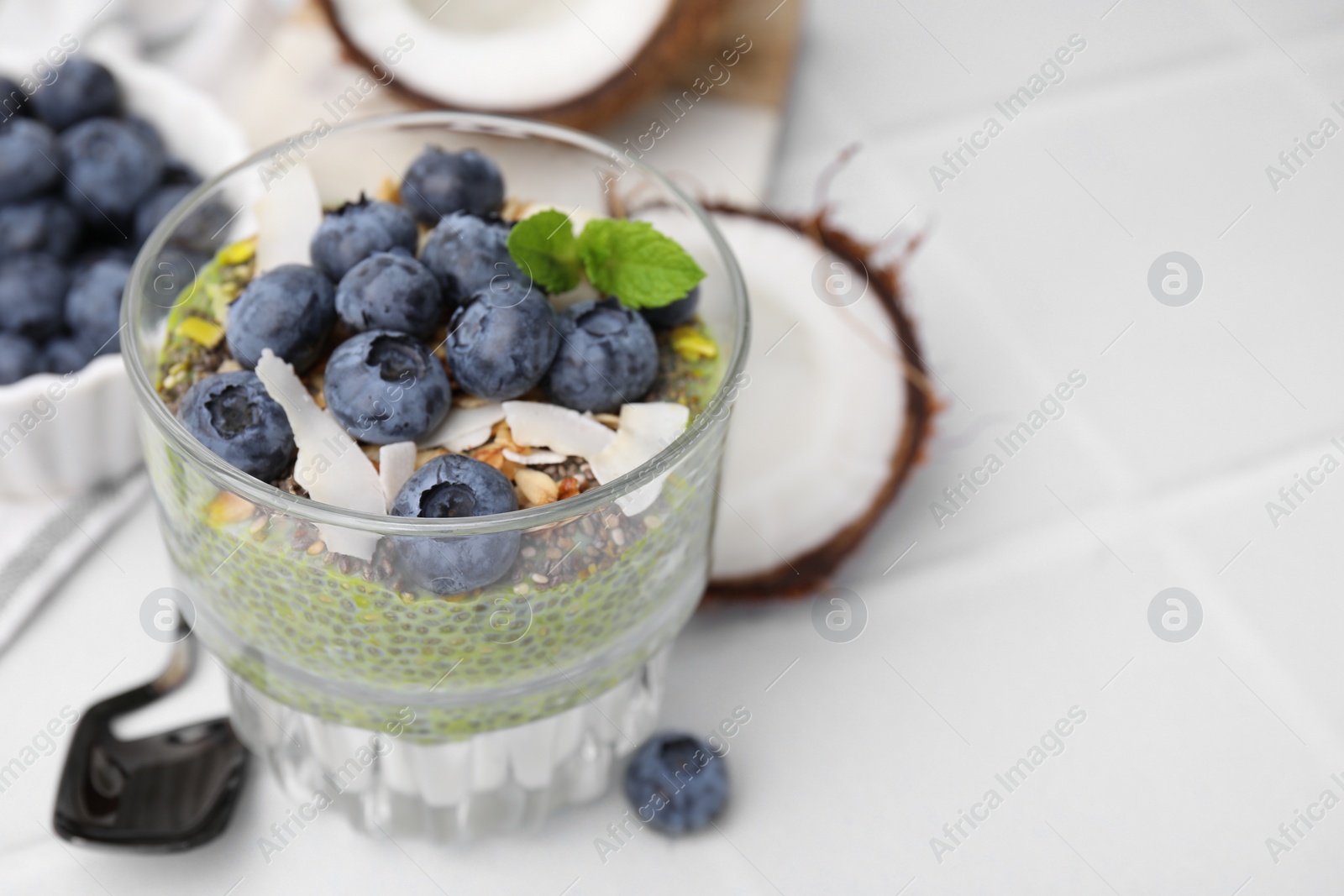 Photo of Tasty chia matcha pudding with coconut and blueberries on white table, space for text. Healthy breakfast