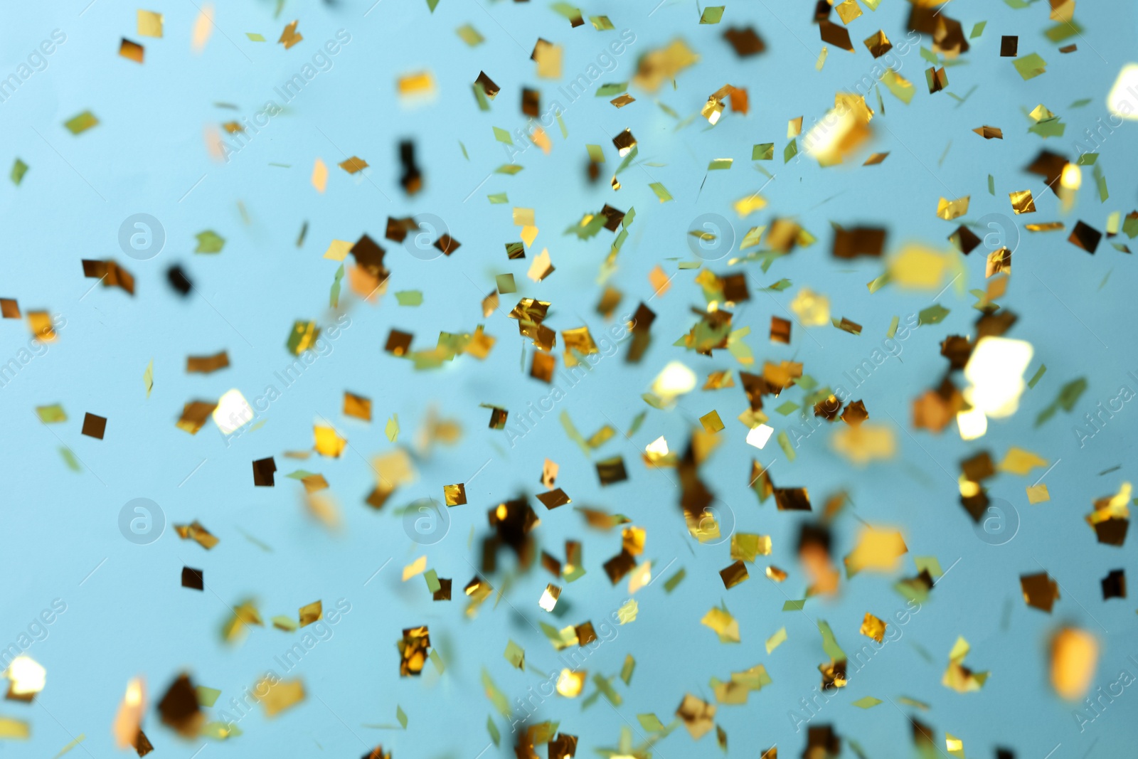 Photo of Shiny golden confetti falling down on light blue background