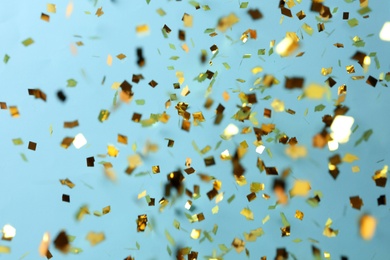 Photo of Shiny golden confetti falling down on light blue background