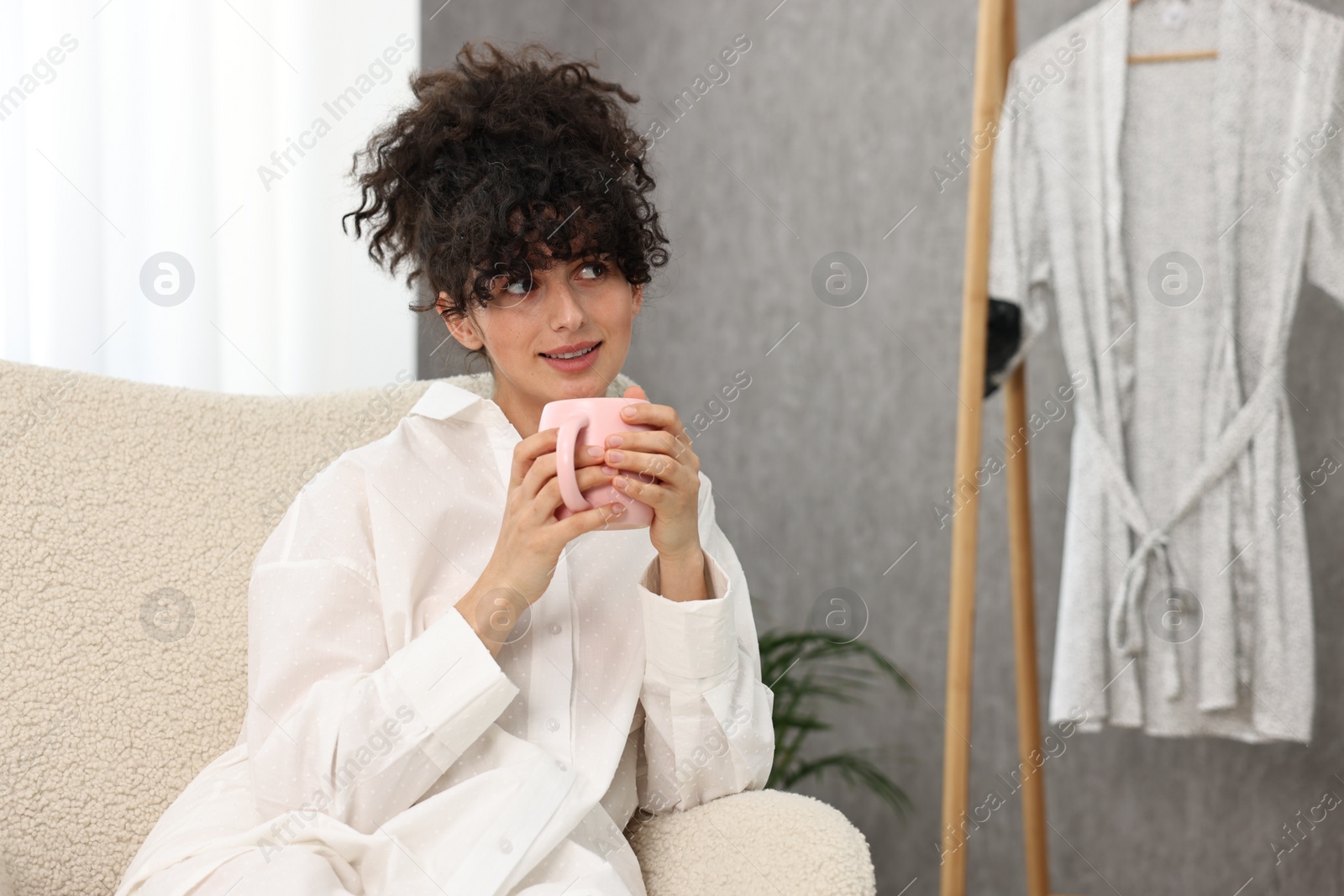 Photo of Beautiful young woman in stylish pyjama with cup of drink at home