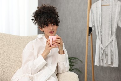 Beautiful young woman in stylish pyjama with cup of drink at home