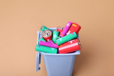 Many used batteries in recycling bin on light brown background