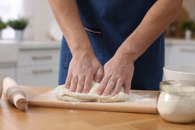 Photo of Making bread. Man kneading dough at wooden table in kitchen, closeup