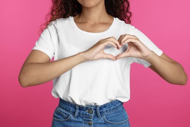 Photo of African-American woman making heart with hands on pink background, closeup