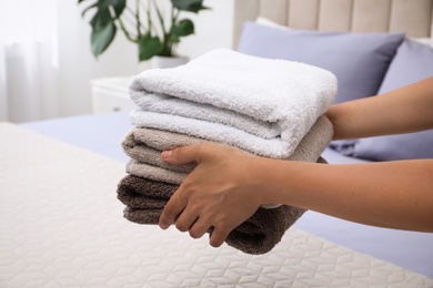 Photo of Woman putting Soft clean terry towels on bed, closeup