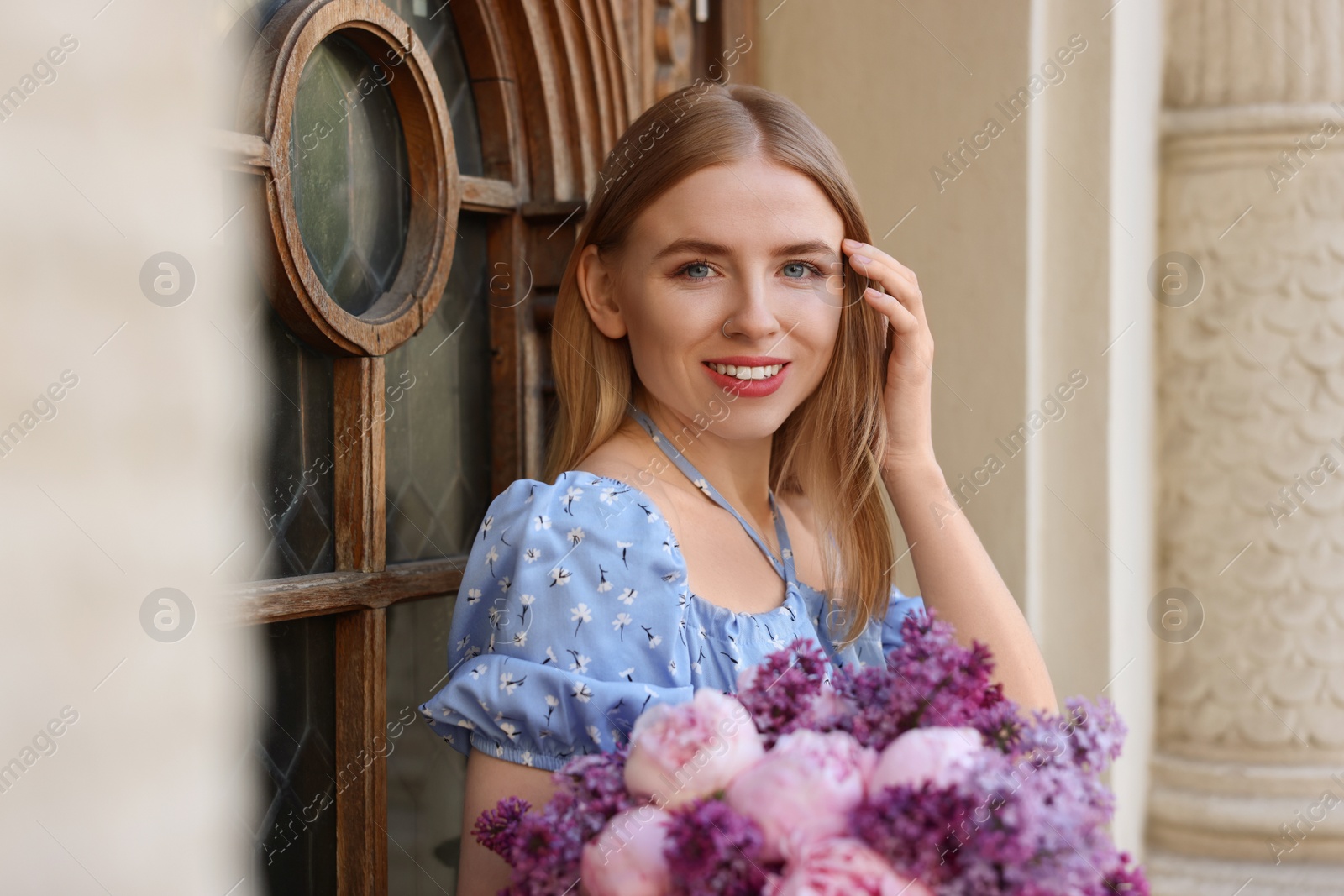 Photo of Beautiful woman with bouquet of spring flowers near building outdoors