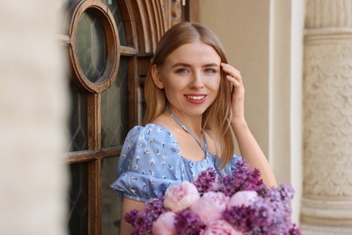 Photo of Beautiful woman with bouquet of spring flowers near building outdoors