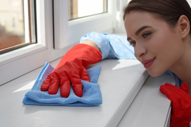 Photo of Young woman cleaning window sill with rag at home