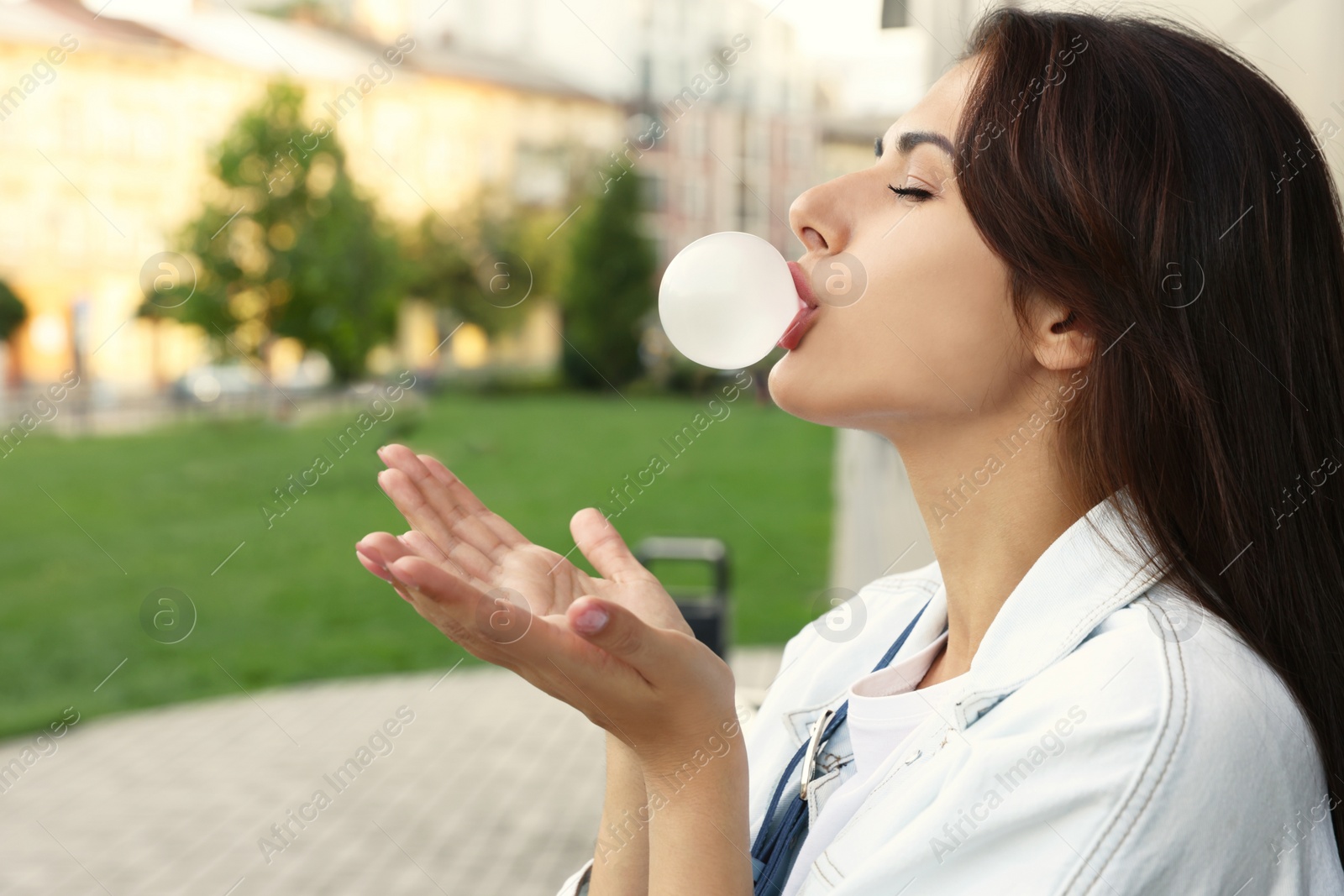 Photo of Stylish young woman blowing gum in park