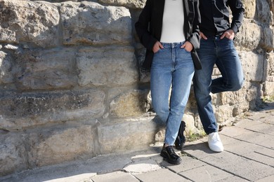 Photo of People in stylish jeans near stone wall outdoors on sunny day, closeup. Space for text