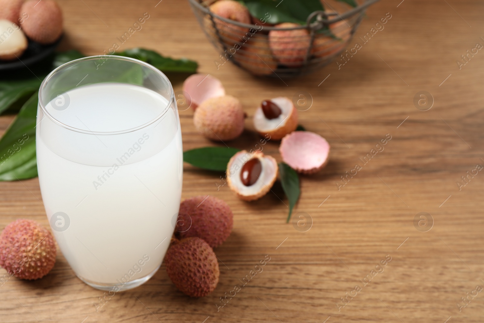 Photo of Lychee juice and fresh fruits on wooden table. Space for text