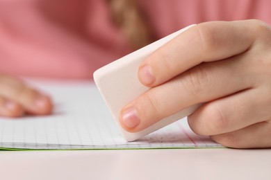 Photo of Girl using eraser at white desk, closeup