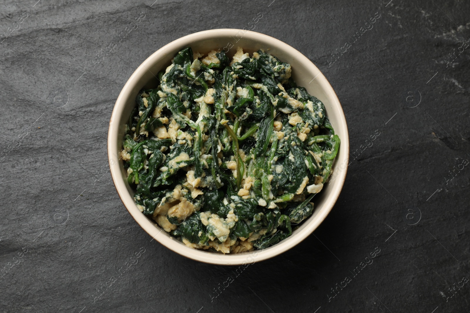 Photo of Tasty spinach dip with egg in bowl on black table, top view