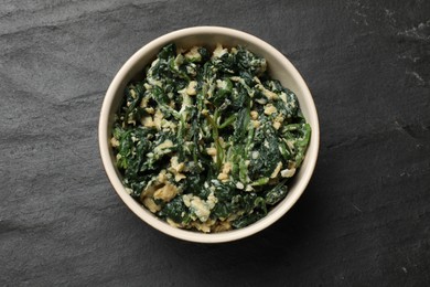 Photo of Tasty spinach dip with egg in bowl on black table, top view