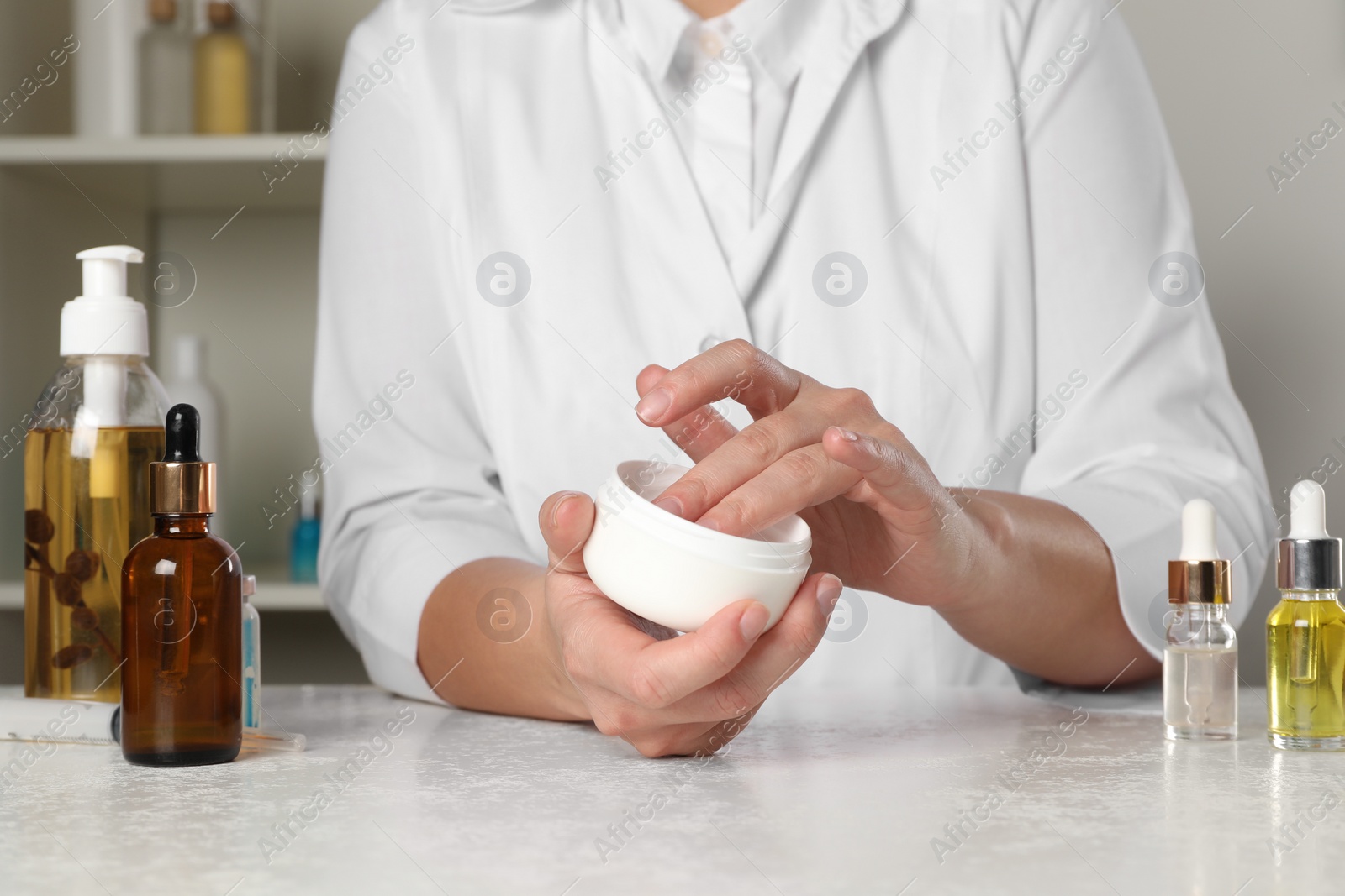 Photo of Dermatologist testing cosmetic product at white table indoors, closeup