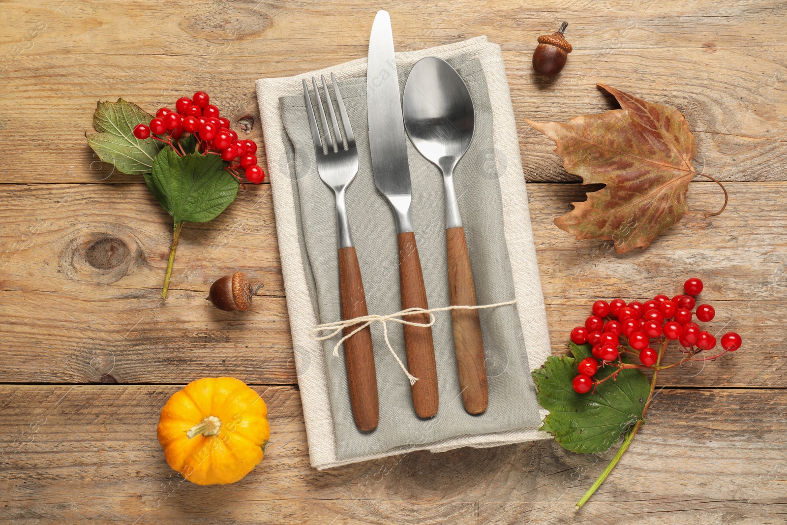 Photo of Autumn table setting. Cutlery, napkins, viburnum berries and pumpkin on wooden background, flat lay