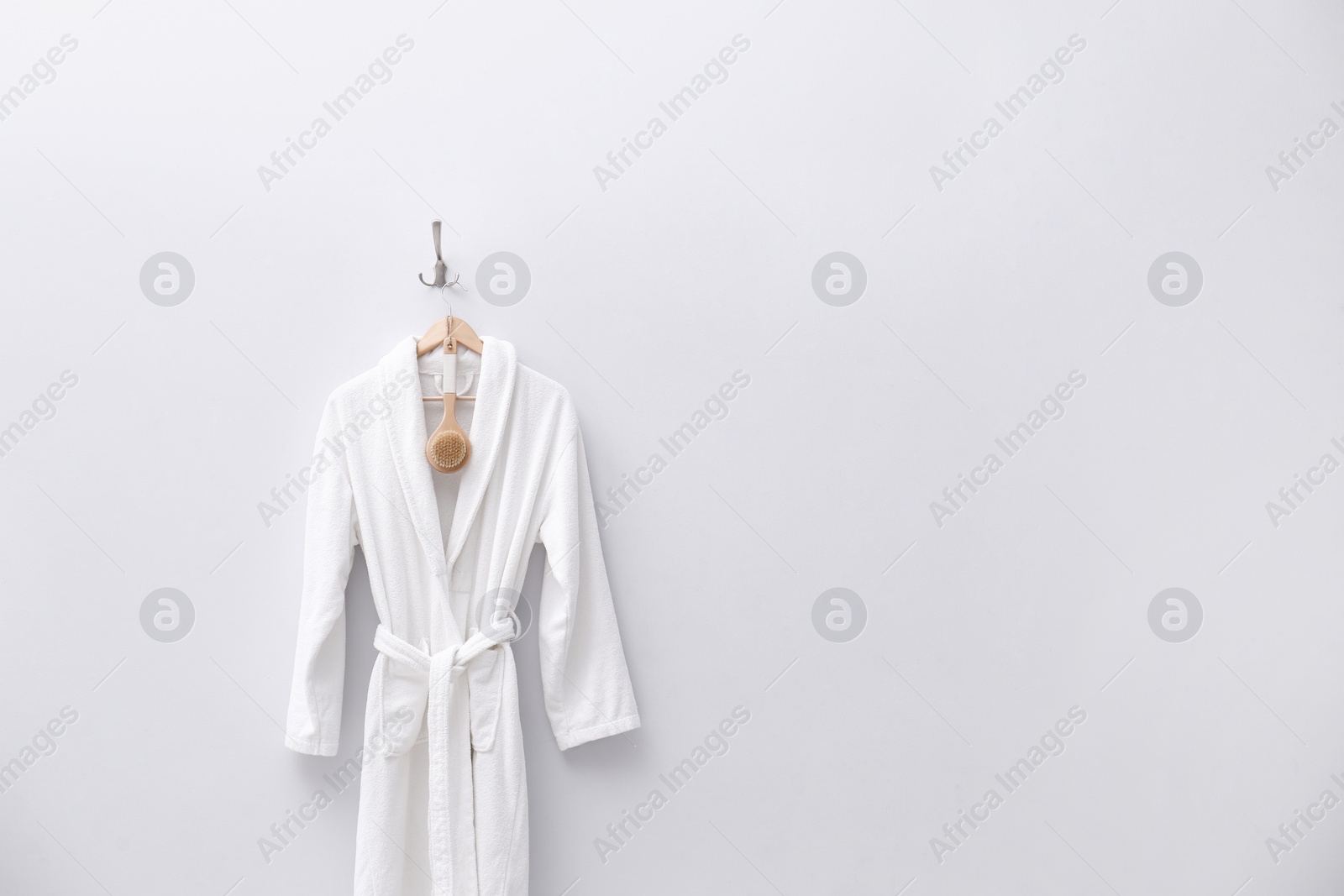 Photo of Fresh white bathrobe hanging on light wall. Space for text