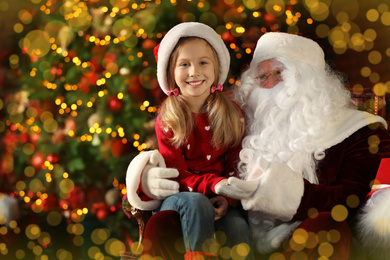 Photo of Santa Claus and little girl near Christmas tree indoors