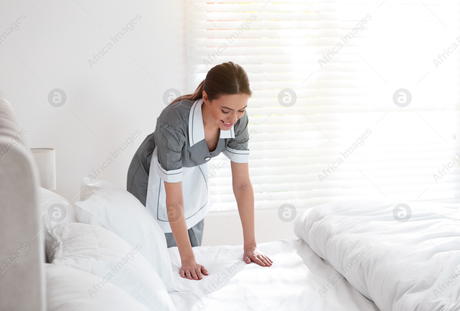 Photo of Young chambermaid making bed in hotel room