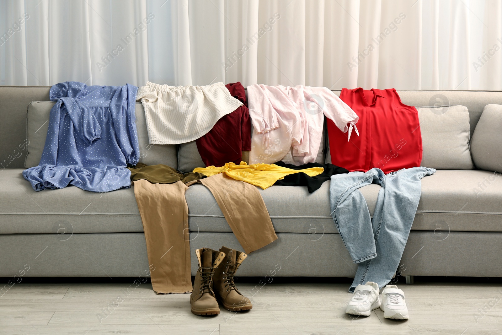 Photo of Shoes near sofa with different clothes indoors