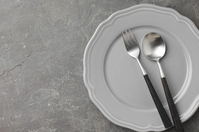 Photo of Stylish setting with cutlery and plate on grey textured table, top view. Space for text