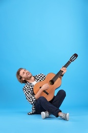 Young man playing acoustic guitar on color background