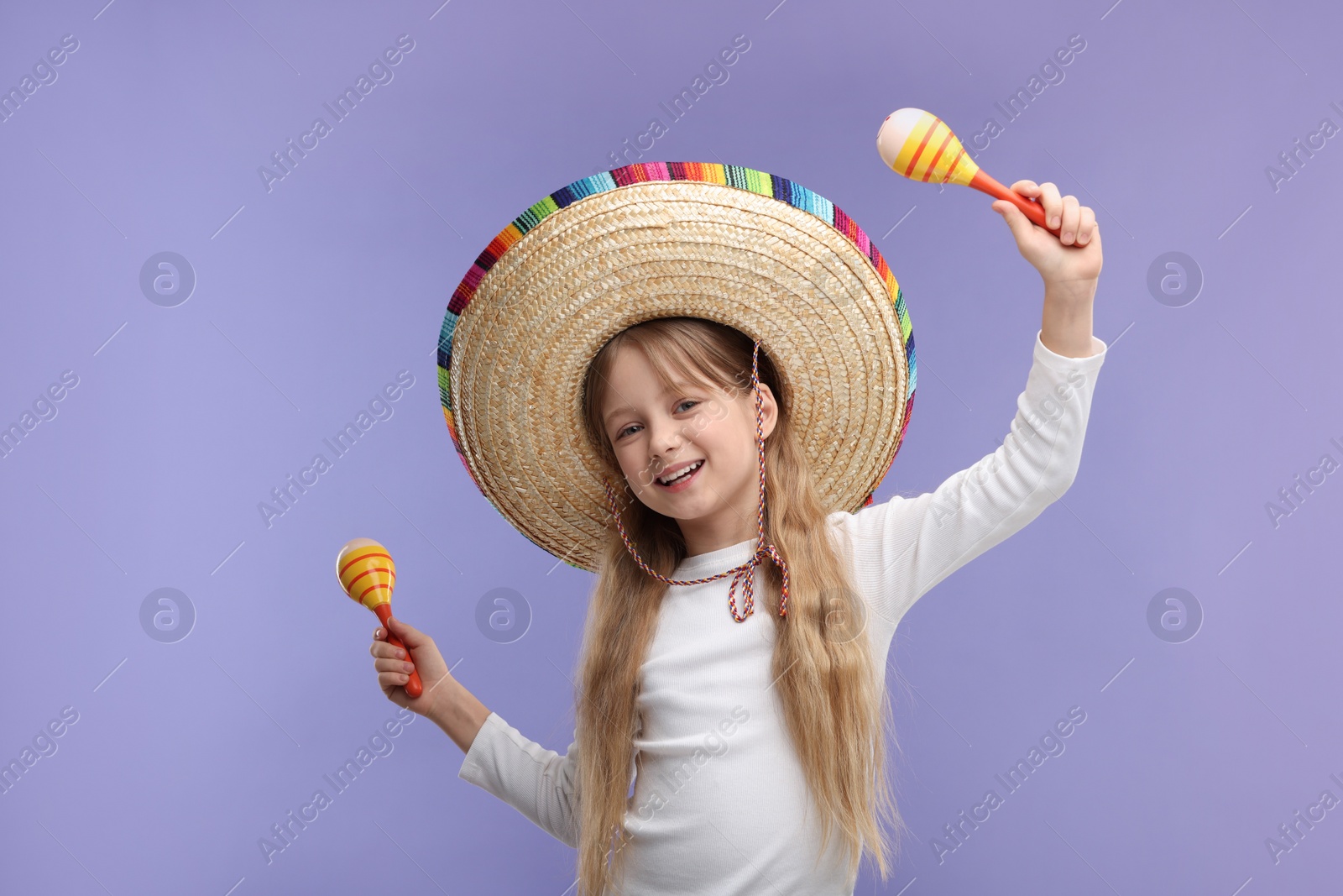 Photo of Cute girl in Mexican sombrero hat dancing with maracas on purple background