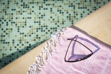 Photo of Stylish sunglasses and blanket near outdoor pool on sunny day, top view. Space for text