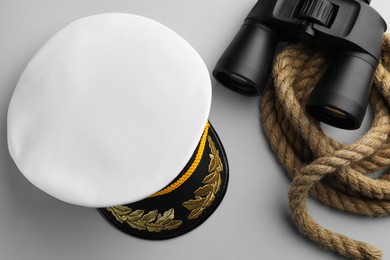 Photo of Peaked cap, rope and binoculars on light grey background, flat lay