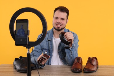 Photo of Smiling fashion blogger showing men's accessories while recording video at table against orange background